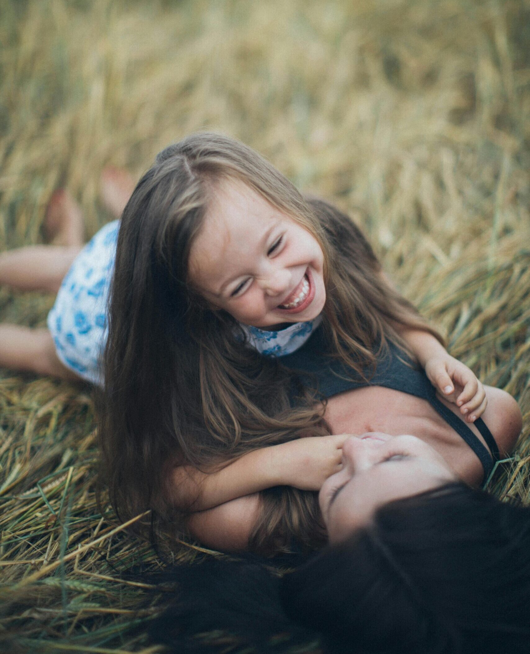 A joyful mother and daughter sharing a playful moment in a sunlit summer field.