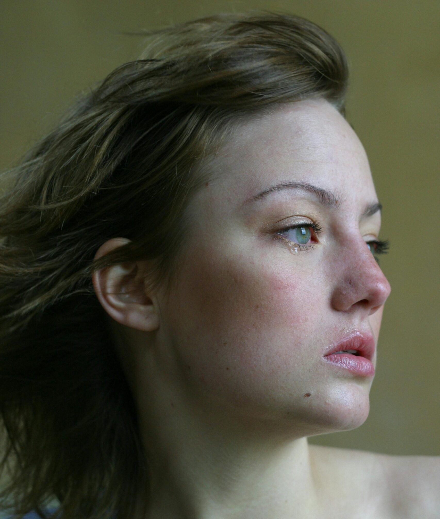 Młoda kobieta na zielonym tle ze łzą w oku. Patrzy w prawo w dal.