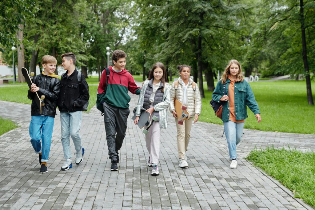 Grupa nastolatków i młodzieży spacerująca po parku, rozmawiająca i budująca pozytywne relacje rówieśnicze.