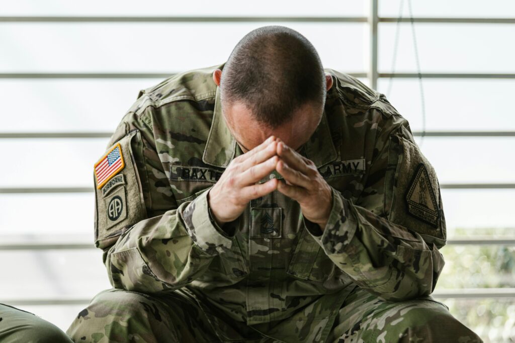 pexels-photo-7468260-7468260 A soldier in camouflage sitting indoors, appearing stressed and overwhelmed.