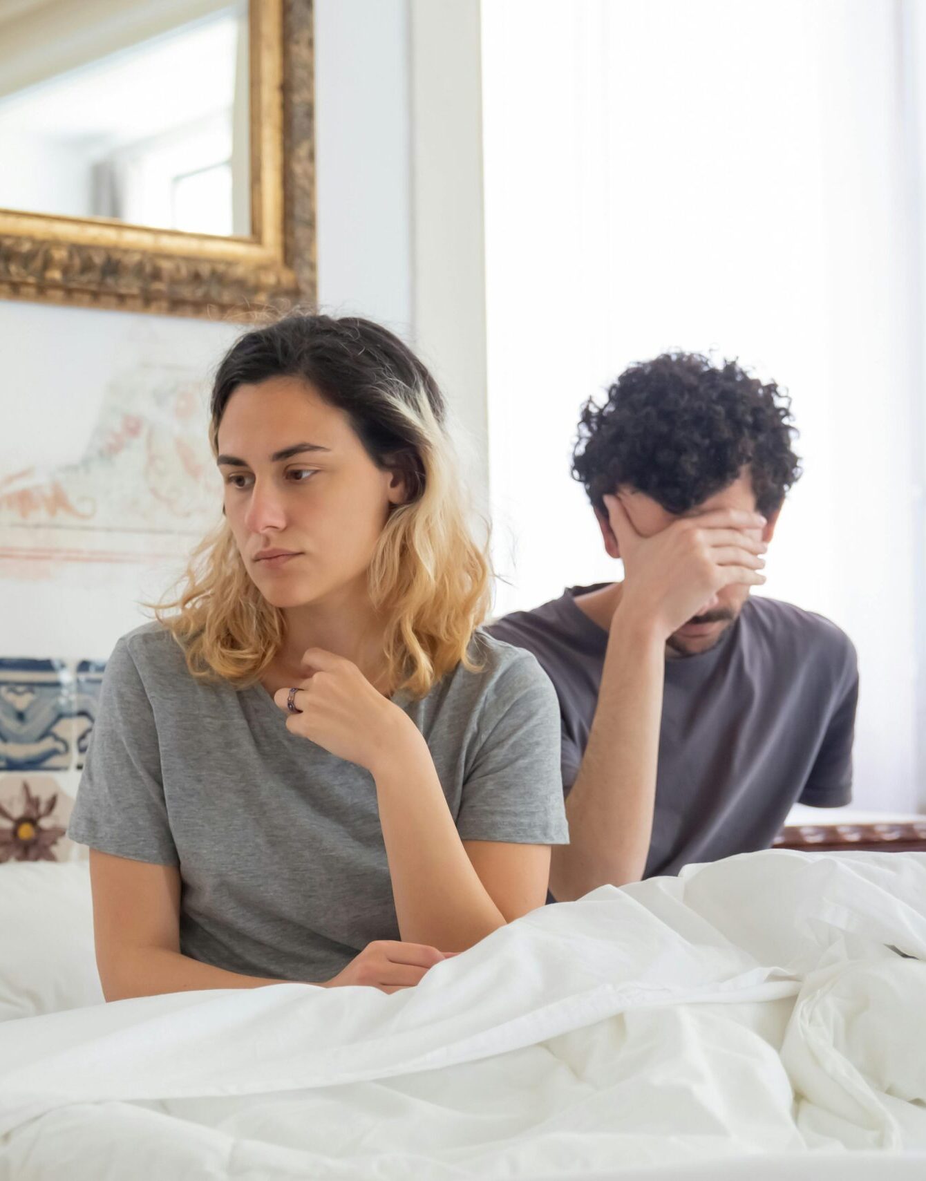 Para siedząca w łóżku, smutna i zamyślona. Widać że się nie dogadują i potrzebują terapii par.