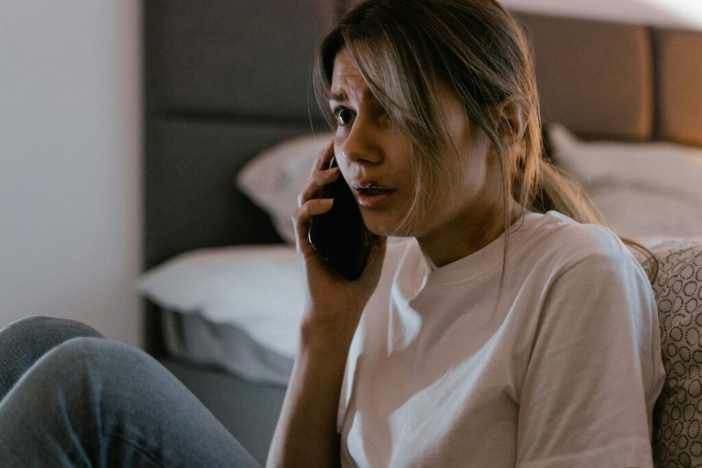 pexels-photo-7699313-7699313 A worried woman in a white shirt making a distressing phone call indoors.