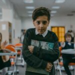 Young boy in school library looking sad while classmates point and laugh.