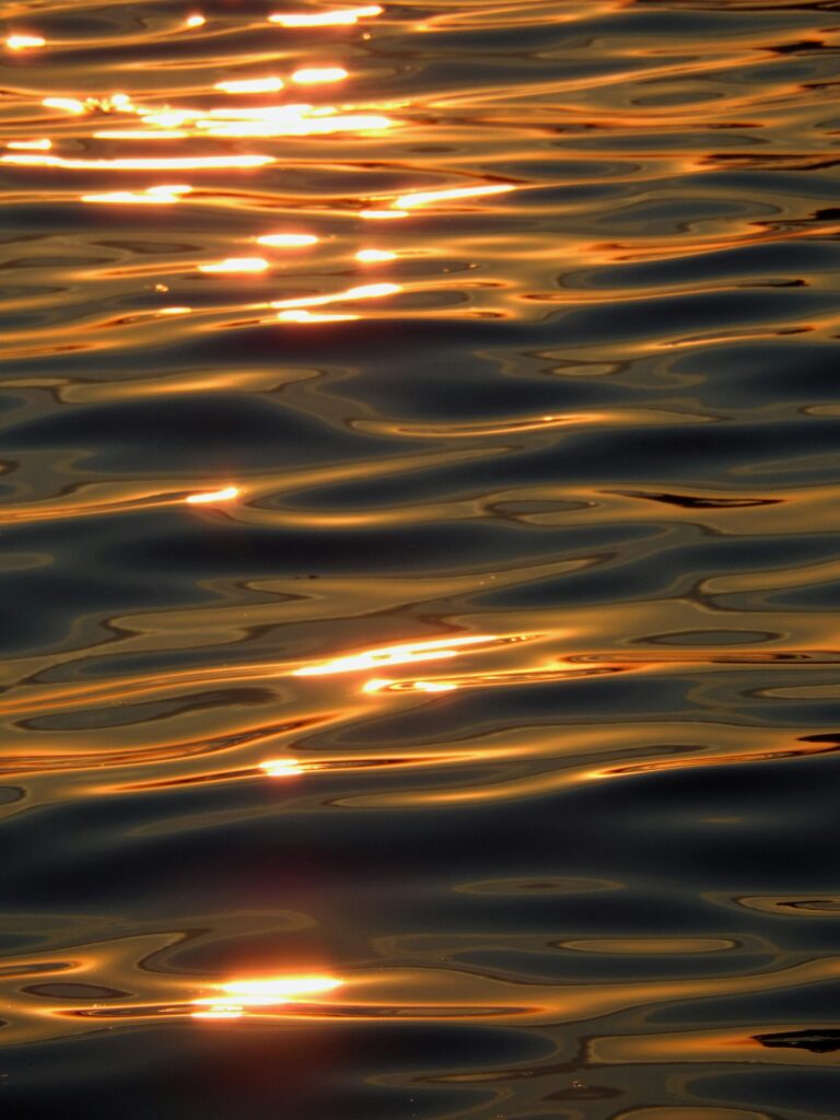 Golden sunlight reflecting on rippling water creates a stunning natural abstract pattern.