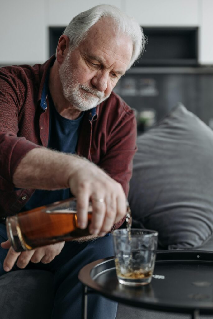 Elderly man pours whiskey into a glass at home, capturing a moment of relaxation.