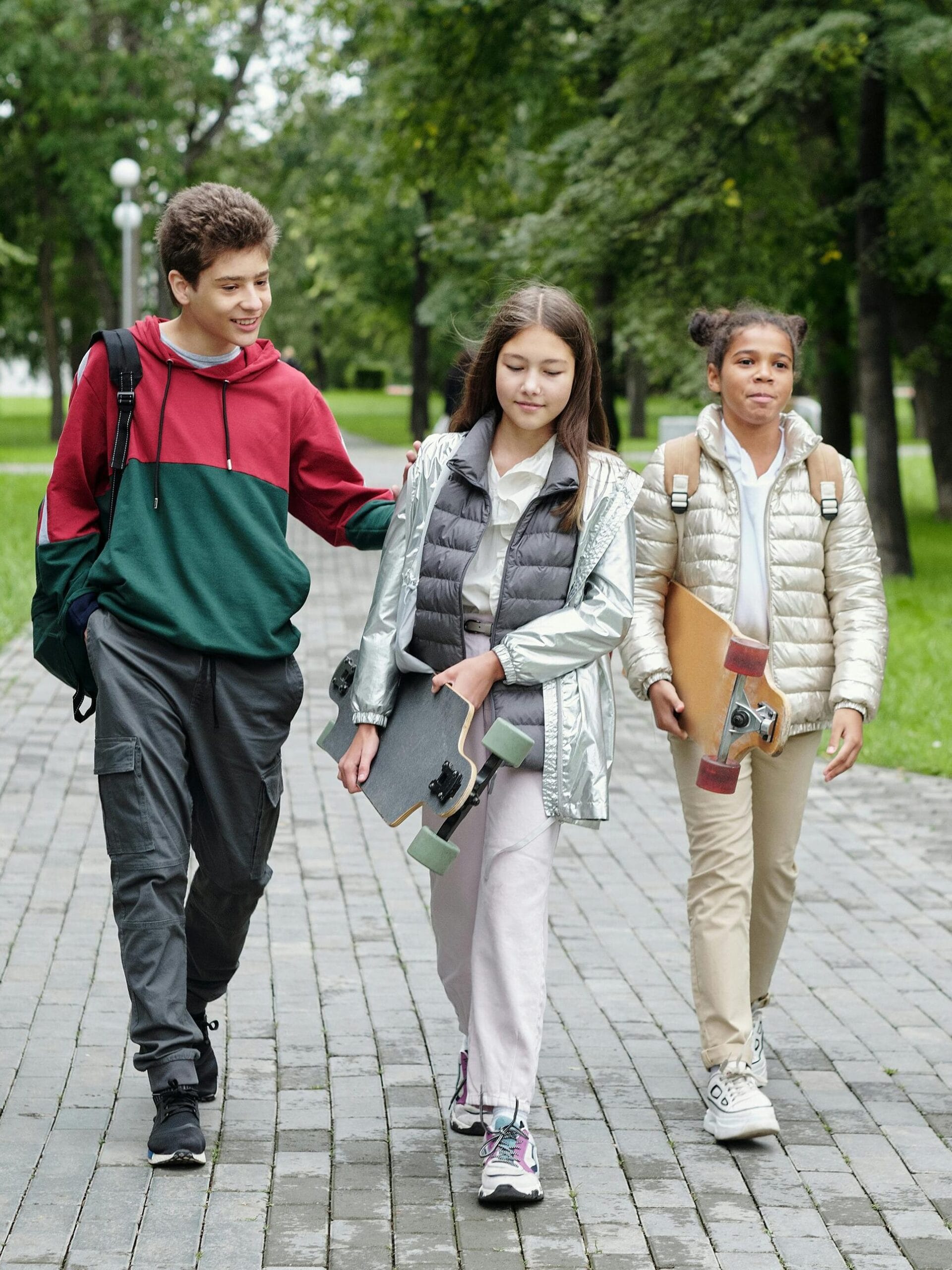 Group of teenagers walking and laughing together in a sunny park setting.