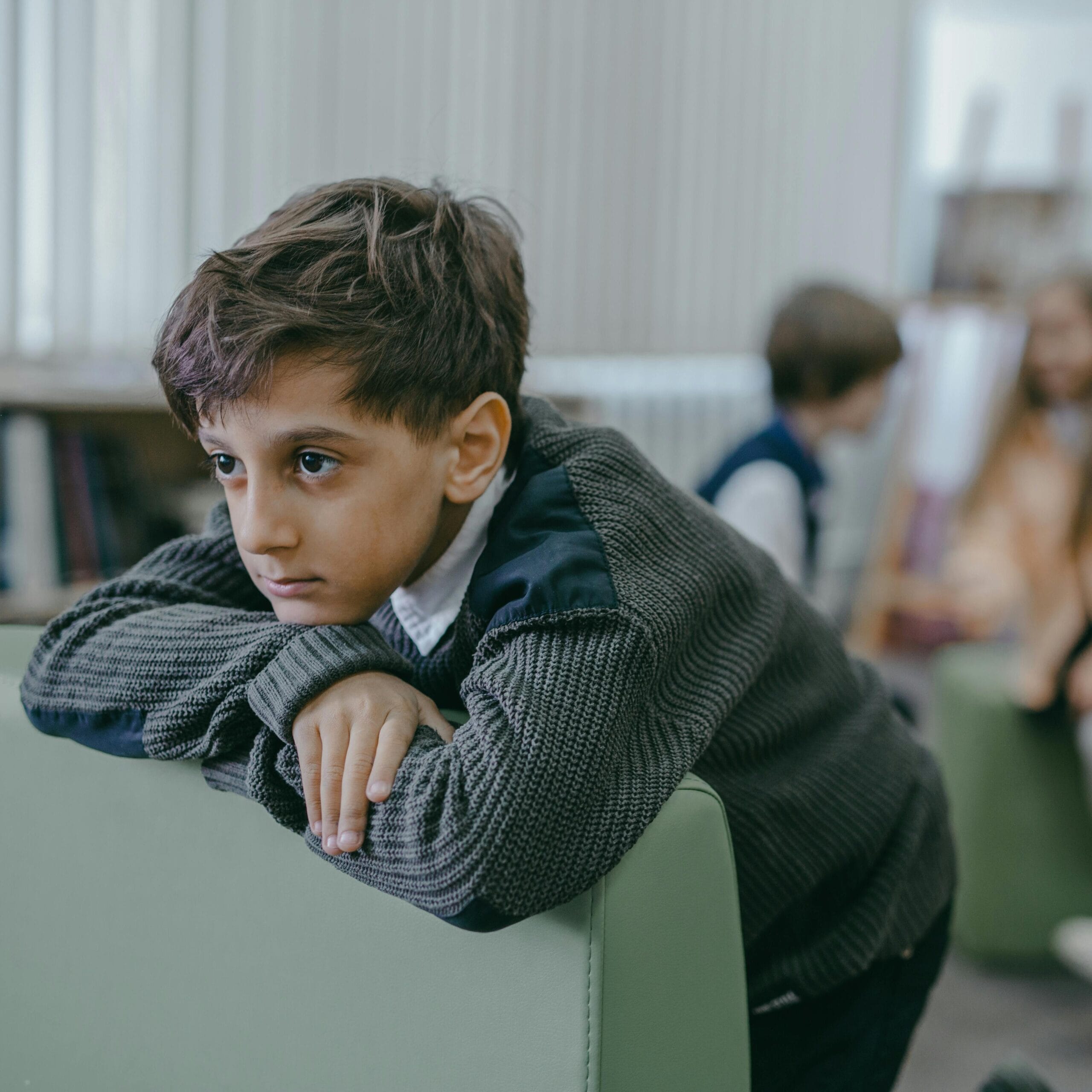A sad boy leans on a chair in a library, highlighting themes of bullying and loneliness.